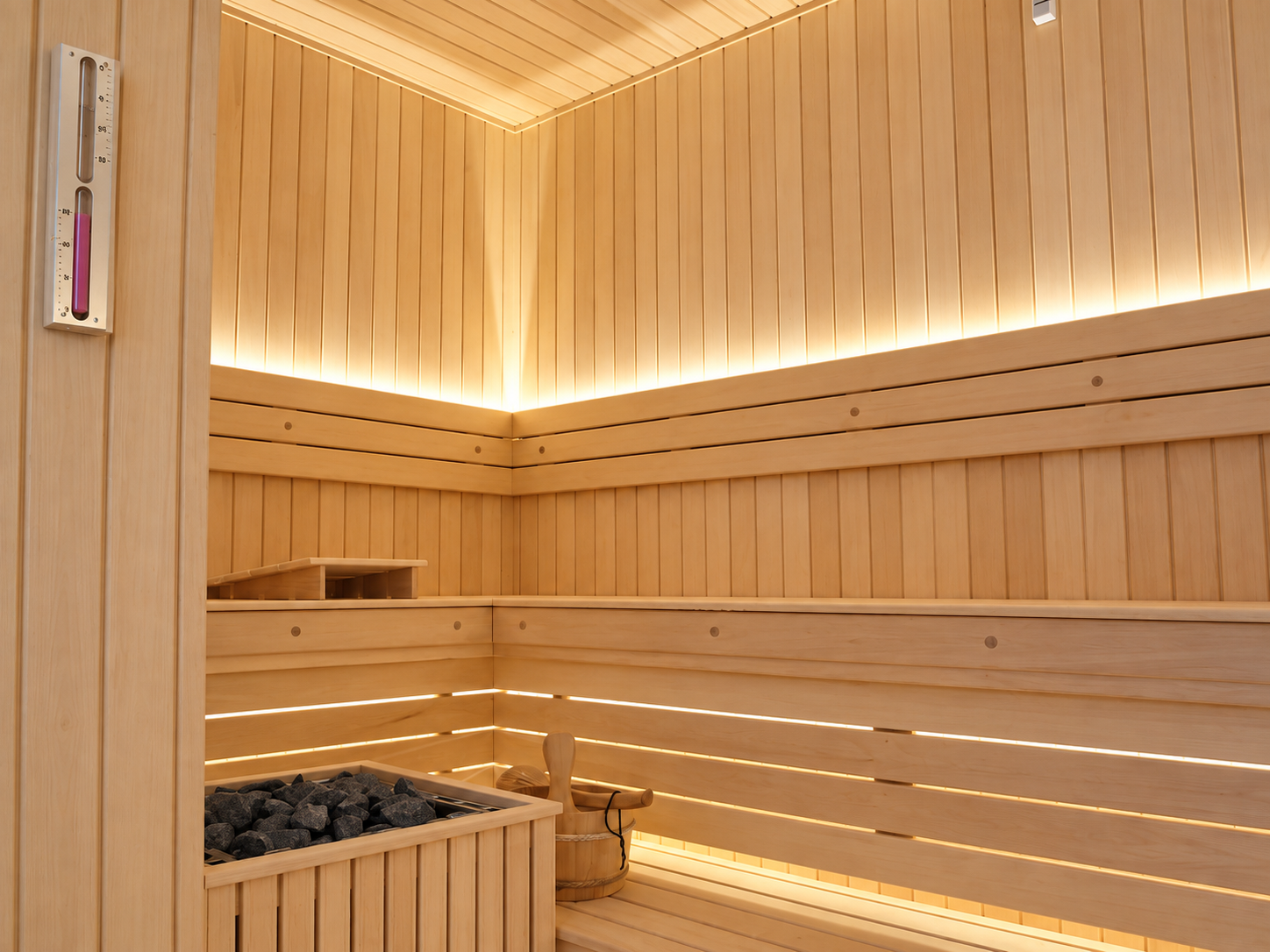 Sauna en bois clair avec éclairage indirect derrière les dossiers et sous les banquettes